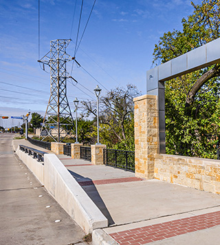 Image include a road on the left, a wide walking path on the right and a transmission line in the background.